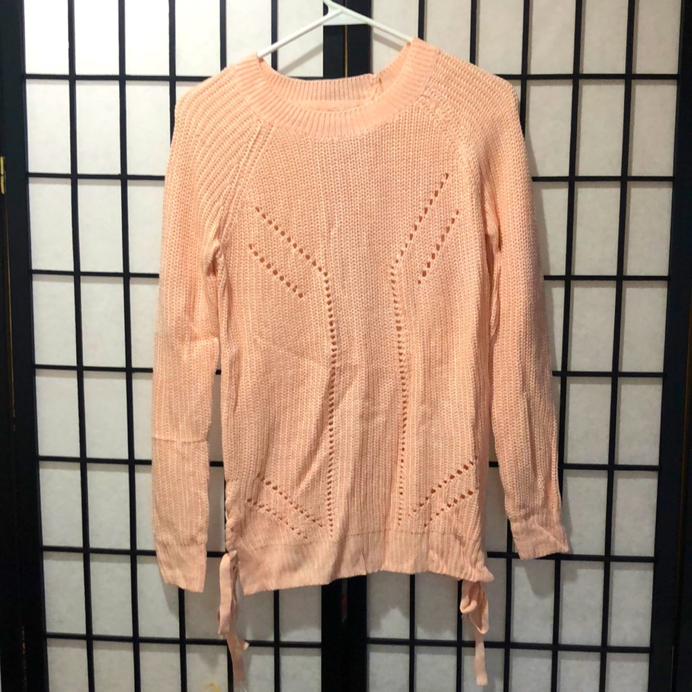A baby pink knit sweater with ribbons on the side